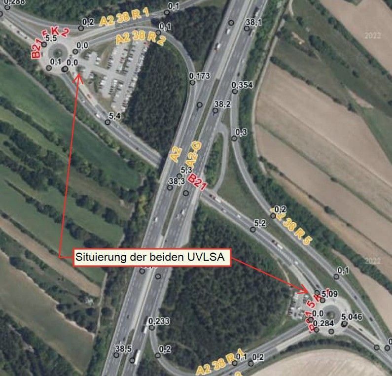 Eine Luftaufnahme einer Autobahnkreuzung mit verschiedenen Zahlen und Codes markiert. Die Beschriftungen umfassen B21, F2 und A2 38 R1, R2. Ein roter Pfeil zeigt auf einen bestimmten Ort, der als 'Situierung der beiden UVLSA' beschriftet ist.