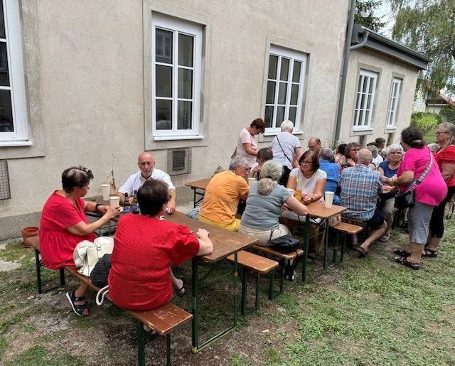 Menschen sitzen an Biergartentischen vor einem Gebäude und unterhalten sich bei einem Fest.