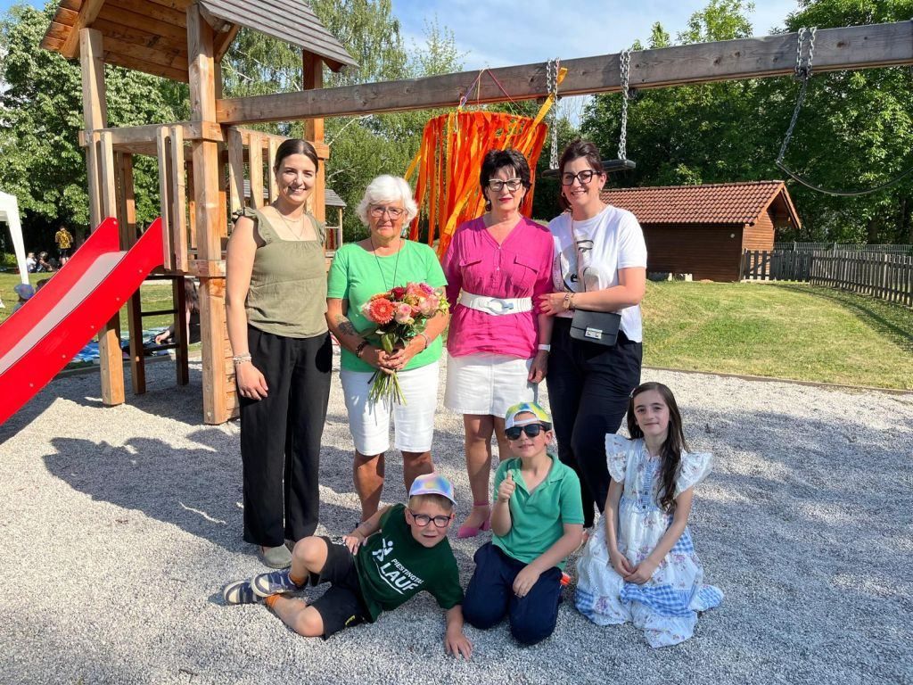 A group of people are posing for a photo at a playground, with one holding a bouquet of flowers.