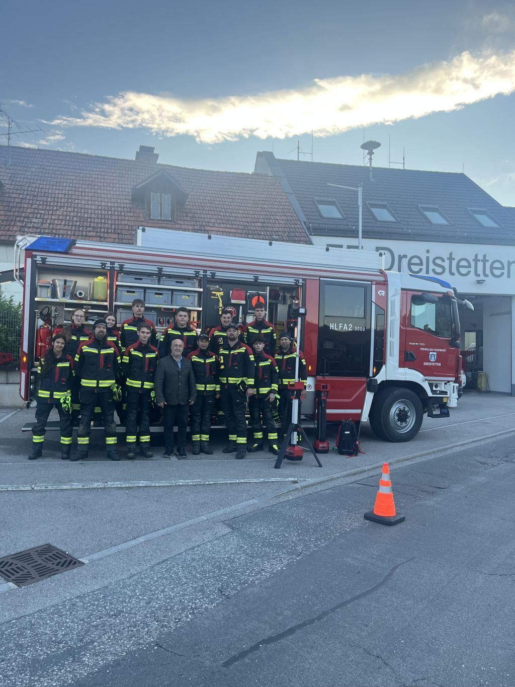 Eine Gruppe Feuerwehrleute in Uniform posiert für ein Foto vor einem Feuerwehrauto. Dahinter steht ein Gebäude mit der Aufschrift Dreistettter.