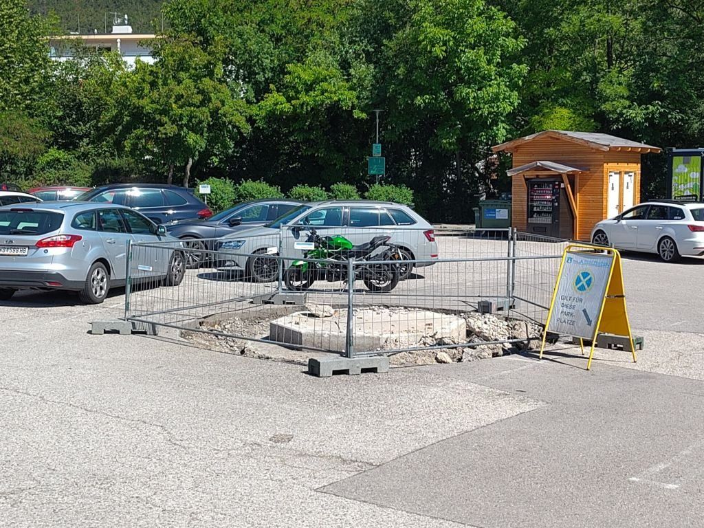 Ein grünes Motorrad in einem eingezäunten Bereich geparkt, mit Autos in der Nähe und einem kleinen Gebäude im Hintergrund.