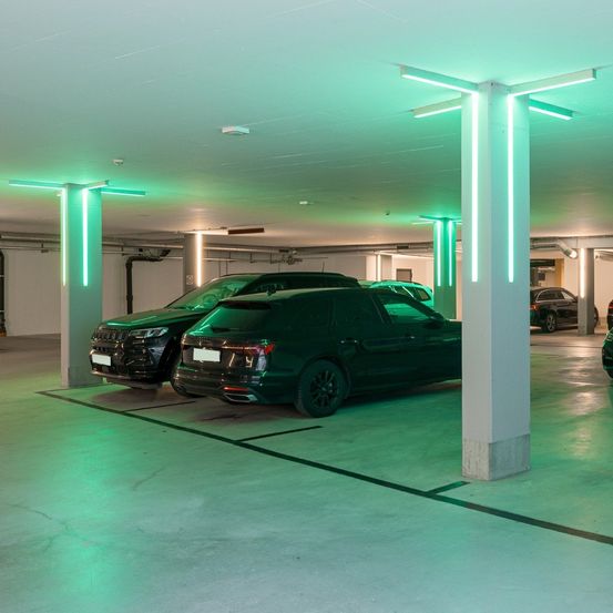 Eine unterirdische Parkgarage mit grünen Lichtern zeigt zwei grüne Autos nebeneinander geparkt, mit weiteren Autos in der Ferne.
