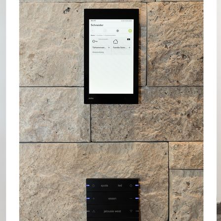 Ein Touchscreen-Gerät ist an einer Steinwand montiert. Der Bildschirm zeigt den Namen Schneider und ein Datum vom 12.28.2016. Es gibt zwei Symbole und das Wort Anwendling. Unter dem Bildschirm befindet sich ein schwarzes rechteckiges Panel mit den Wörtern spots, led, essen und jalousie west.