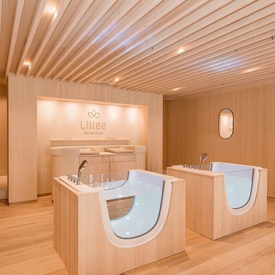 Das Lillee-Spa verfügt über ein hölzerne Inneneinrichtung mit zwei Badewannen, einem Wasserhahn und einem Spiegel. Der Markenname Lillee ist an der Wand angebracht.