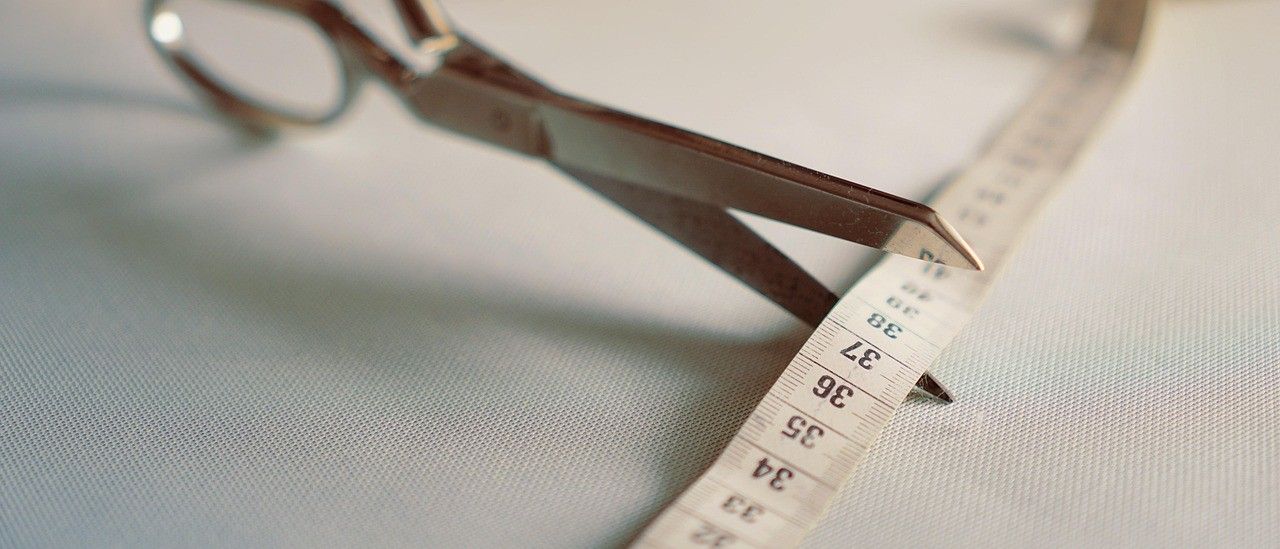 Ein Paar Scheren mit einem Maßband auf einem weißen Tuch. Das Band hat Messungen bis zu 48 Zoll.