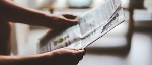 Eine Person hält eine Zeitung und konzentriert sich auf den Text, wobei die Umgebung verwischt ist.