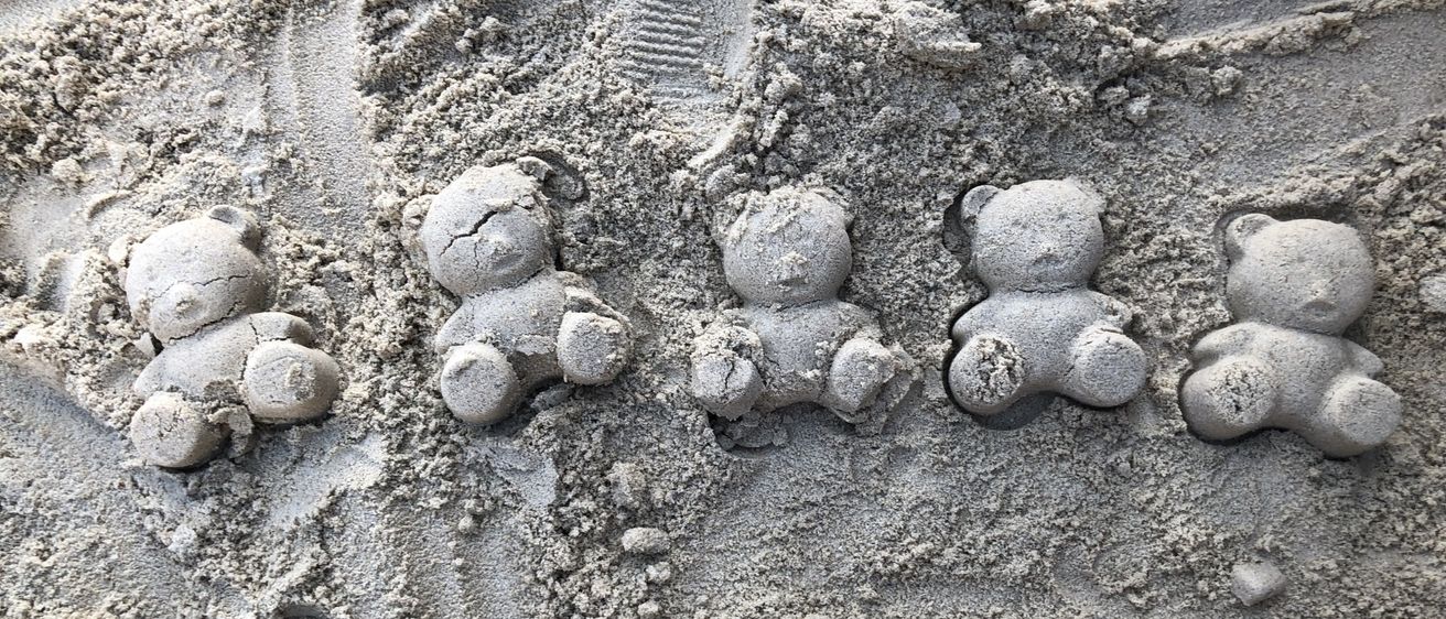 Fünf kleine Bärenstatuen sind aus Sand geformt und in einer Reihe angeordnet, umgeben von Fußabdrücken.