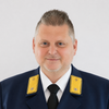 Ein Mann in einem dunkelblauen Uniformanzug mit gelben Aufnähern, einer schwarzen Krawatte und einem weißen Hemd posiert für ein Foto.
