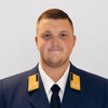 Ein Mann in einer Marineuniform mit goldenen Schulterstücken lächelt für die Kamera, möglicherweise in einem professionellen Umfeld.