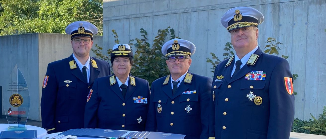 Vier Personen in Militäruniform stehen neben einem Tisch mit Auszeichnungen. Im Hintergrund befindet sich ein Banner mit Text und dem ECOSOC-Logo.