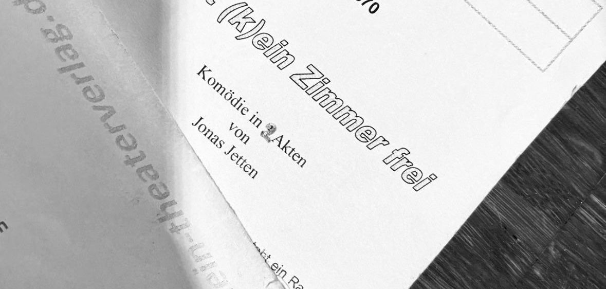 Ein Nahaufnahme eines weißen Papiers mit einem Maskenlogo und schwarzem Text. Das Papier hat einen schwarzen Rand und liegt auf einer Holzoberfläche. Der Text lautet 'In Knast ist (k)jein Zimmer frei.' Das Papier hat auch einen kleinen weißen Maskenaufkleber.