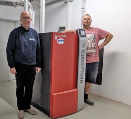 Zwei Männer stehen neben einem großen rot-schwarzen Gerät in einem Raum und lächeln für die Kamera.