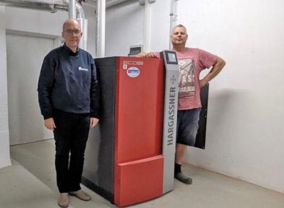 Zwei Männer stehen neben einem großen rot-schwarzen Gerät in einem Raum und lächeln für die Kamera.