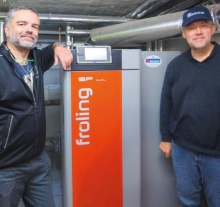 Zwei Männer stehen neben einer großen orange-grauen Maschine mit der Aufschrift 'Froind'. Ein Mann berührt die Maschine, während der andere in die Kamera schaut.