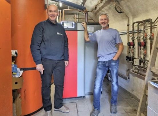 Zwei Männer stehen in einem Raum mit Heizgeräten, lächeln und posieren für ein Foto.