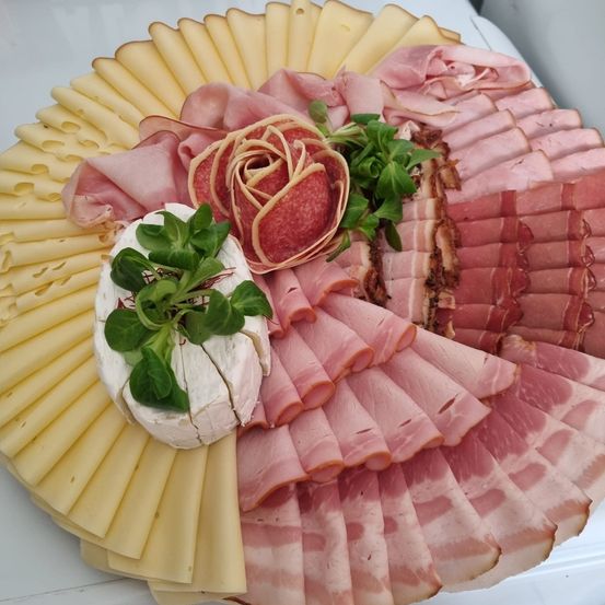 Ein Tablett zeigt verschiedene geschnittene Fleischsorten, darunter Schinken und Salami, neben Käsescheiben und einer dekorativen Rose.