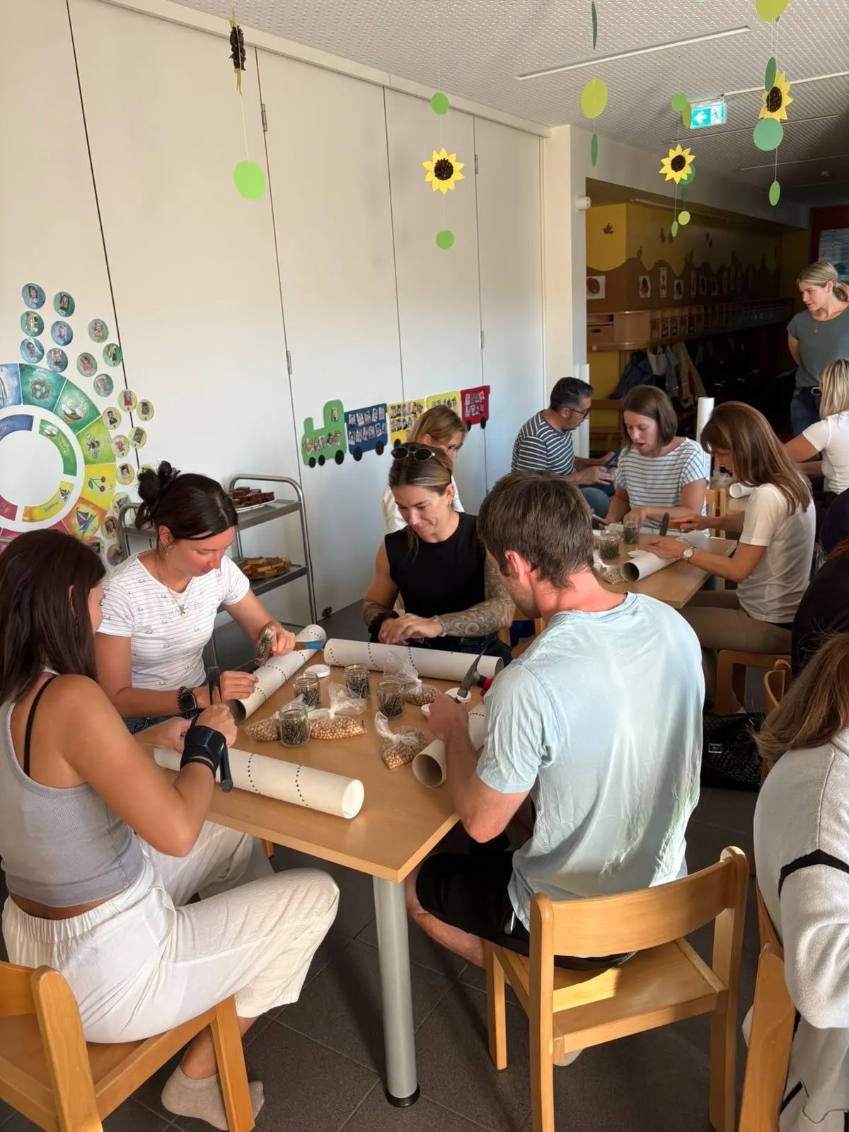 Eine Gruppe von Menschen sitzt in einem Raum um einen Tisch herum und arbeitet an einem Bastelprojekt mit verschiedenen Materialien.