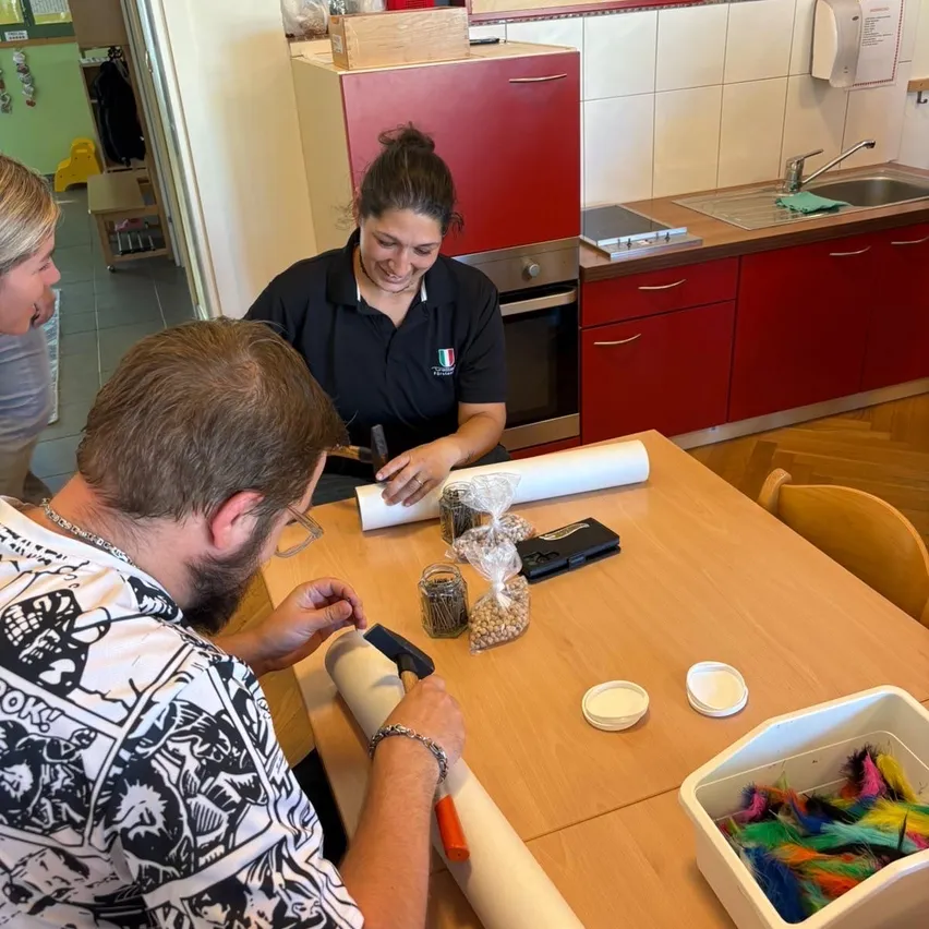 Ein Mann und eine Frau arbeiten gemeinsam an einem Holztisch in einer Küche, umgeben von verschiedenen Gegenständen und Materialien.