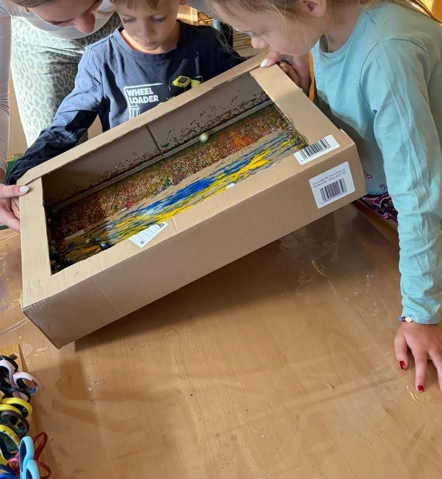 Drei Kinder betrachten eine Pappschachtel voller bunter Wolle.