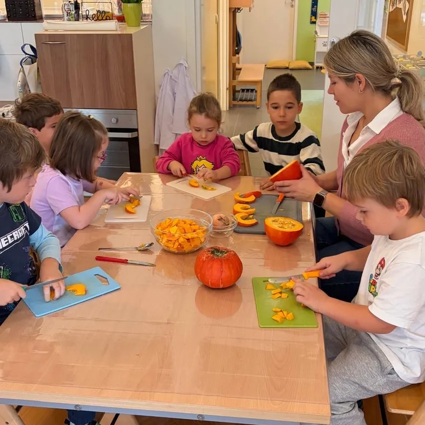 Eine Gruppe von Kindern und einem Erwachsenen sitzen um einen Tisch herum und schneiden Kürbisse.