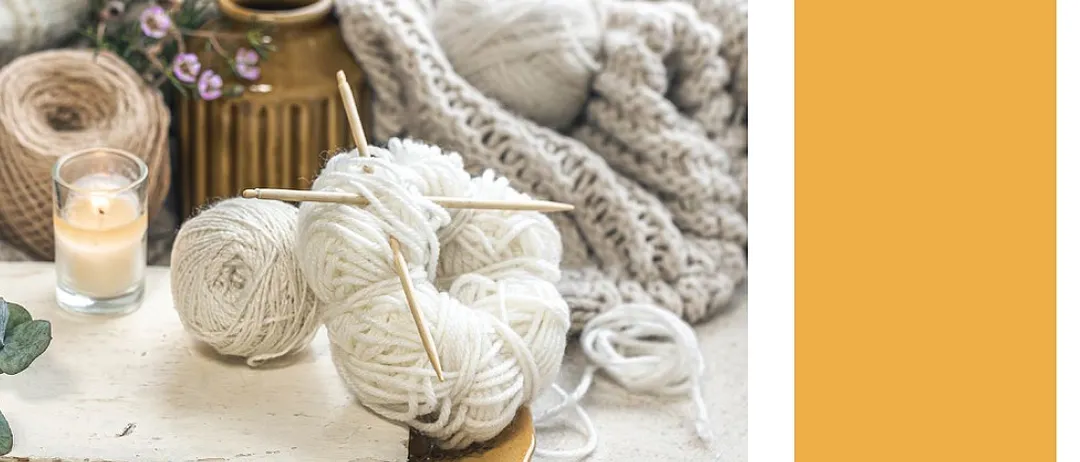 A cozy craft cafe event poster featuring a plate of yarn, knitting needles, a candle, and a knitted blanket. The text reads 'Handarbeits-Cafe'.