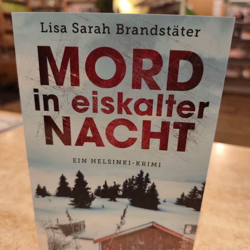 Ein Buch mit dem Titel 'Mord in eiskalter Nacht' von Lisa Sarah Brandstätter. Es ist ein Helsinki-Krimi. Das Cover zeigt eine verschneite Landschaft mit einem Haus und Bäumen.