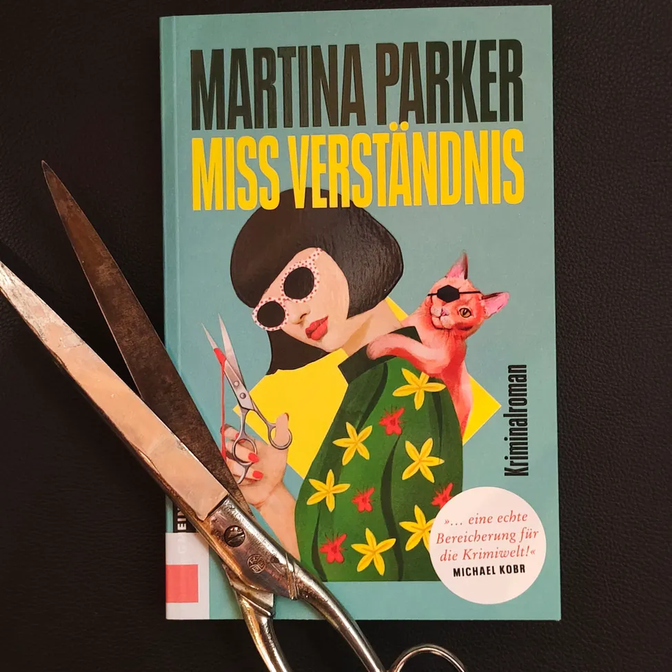 A book titled 'Martina Parker Miss Verstandnis' with a woman in a yellow dress and a cat on her shoulder. A pair of scissors is cutting the book's cover.