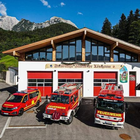 Drei rote Feuerwehrfahrzeuge sind vor einer Feuerwache mit Glasfenstern geparkt, vor dem Hintergrund von Bergen.