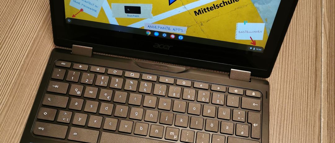 Ein Acer Laptop zeigt eine Karte mit dem Text 'Mittelschule 2 Haid' auf dem Bildschirm. Der Bildschirm zeigt eine Sprechblase mit Anweisungen, wie man wichtige Links in Chrome findet. Der Laptop steht auf einer Holzoberfläche.