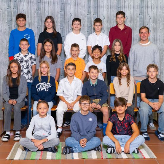 Eine Gruppe junger Personen, sowohl Jungen als auch Mädchen, sitzen und stehen gemeinsam in einem Klassenzimmer und posieren für ein Foto.