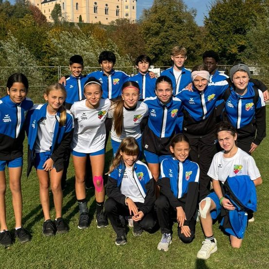 Eine Gruppe junger Athleten in blauen und weißen Uniformen posiert für ein Foto auf einem Feld mit einem Schloss im Hintergrund.