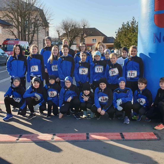 Eine Gruppe von Kindern und Jugendlichen in blauen Uniformen mit Nummern posiert für ein Foto auf der Straße, mit Gebäuden und Bäumen im Hintergrund.