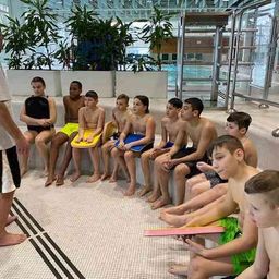 Ein Schwimmlehrer gibt einer Gruppe von Kindern, die auf einer Bank in einem Schwimmbadbereich sitzen, eine Lektion.