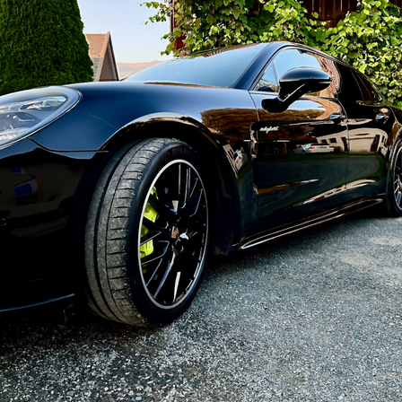 Ein schwarzer Porsche Panamera Sportwagen steht auf Kies. Das Auto zeichnet sich durch ein schlankes Design und einen markanten vorderen Stoßfänger aus.