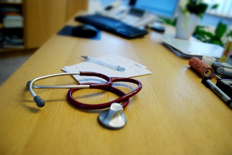 Ein Arztschreibtisch mit Stethoskop, Stift, Notizblock, Tastatur und Topfpflanze auf einem Regal.