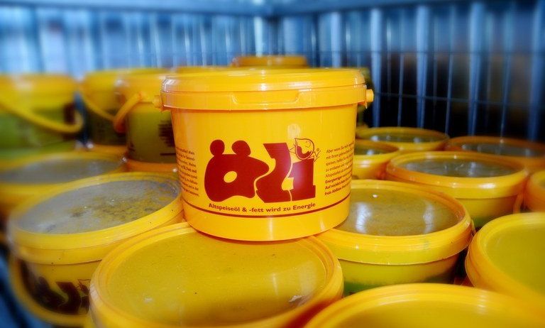 Stapel gelber Eimer mit der Aufschrift 'Q1', in einem Lagerbereich mit einem Metallzaun im Hintergrund.