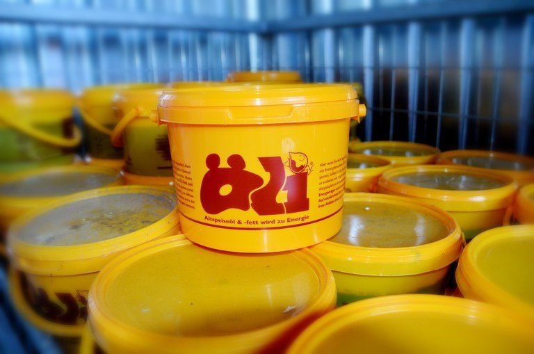 Stapel gelber Eimer mit der Aufschrift 'Q1', in einem Lagerbereich mit einem Metallzaun im Hintergrund.