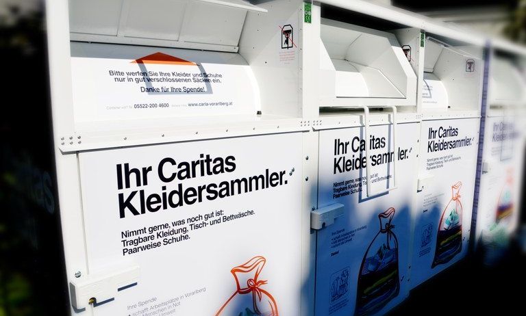 Eine Reihe weißer Spendenboxen für die Kleidersammlung durch Caritas. Jede Box hat den Text 'Ihr Caritas Kleidersammler' und eine Illustration eines Beutels mit Kleidung.