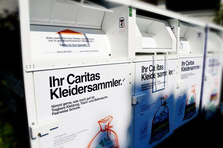 Eine Reihe weißer Spendenboxen für die Kleidersammlung durch Caritas. Jede Box hat den Text 'Ihr Caritas Kleidersammler' und eine Illustration eines Beutels mit Kleidung.