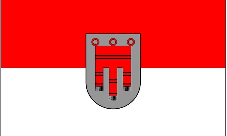 Die Flagge zeigt einen roten und weißen horizontalen Streifen mit einem grauen Schild in der Mitte. Der Schild hat ein rotes und graues Design.