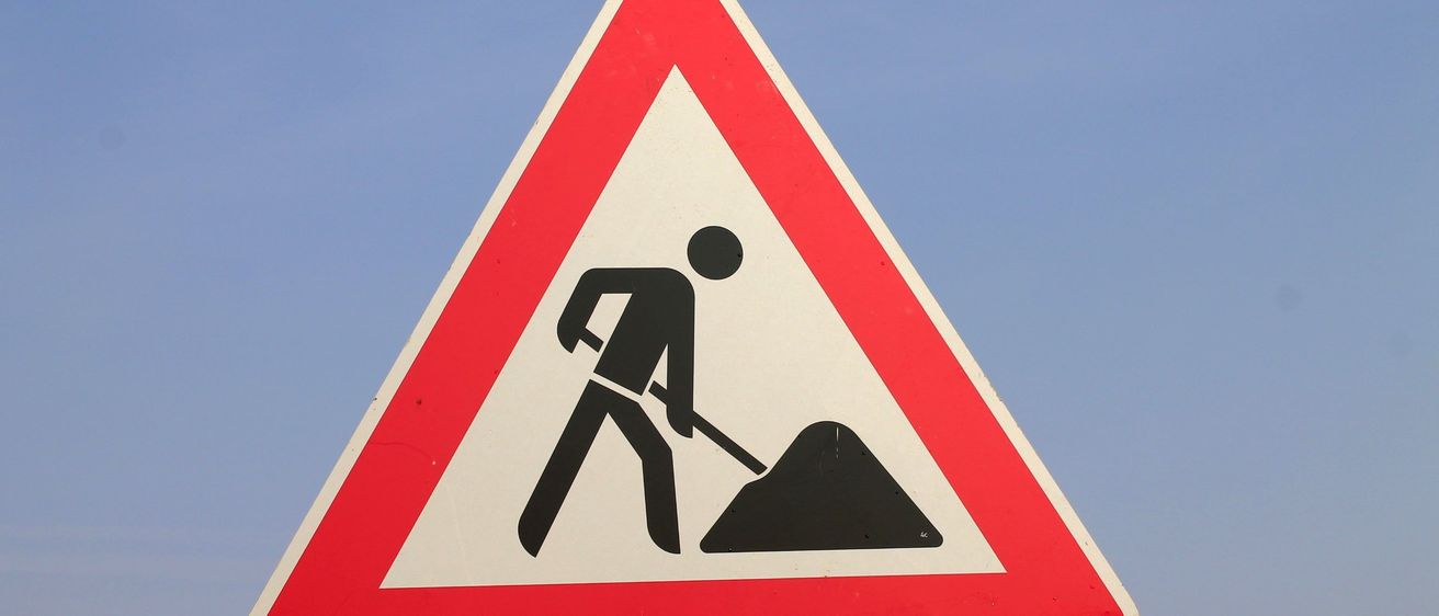 Ein dreieckiges Straßenschild mit einem Mann, der ein Loch gräbt, was auf bevorstehende Straßenarbeiten hinweist.