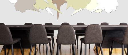 Ein Konferenzraum mit einem langen Tisch und Stühlen, an einer Wand mit verschiedenen farbigen Sprechblasen.