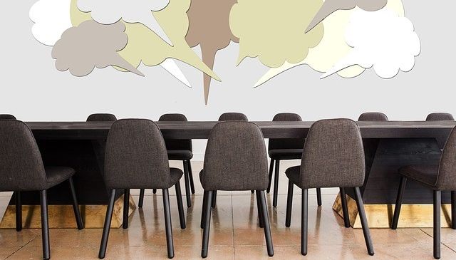 Ein Konferenzraum mit einem langen Tisch, umgeben von Stühlen. An der Wand befinden sich Sprechblasen in verschiedenen Farben.