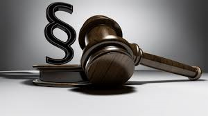 A wooden gavel rests on a book with the letter S in front of it. The gavel is brown and the book is black.