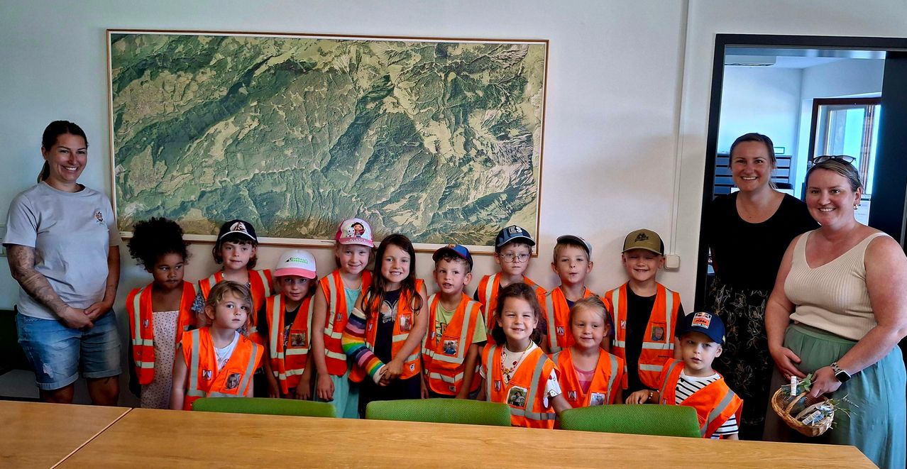 Eine Gruppe von Kindern in orangefarbenen Warnwesten posiert für ein Foto vor einer großen Karte an der Wand.