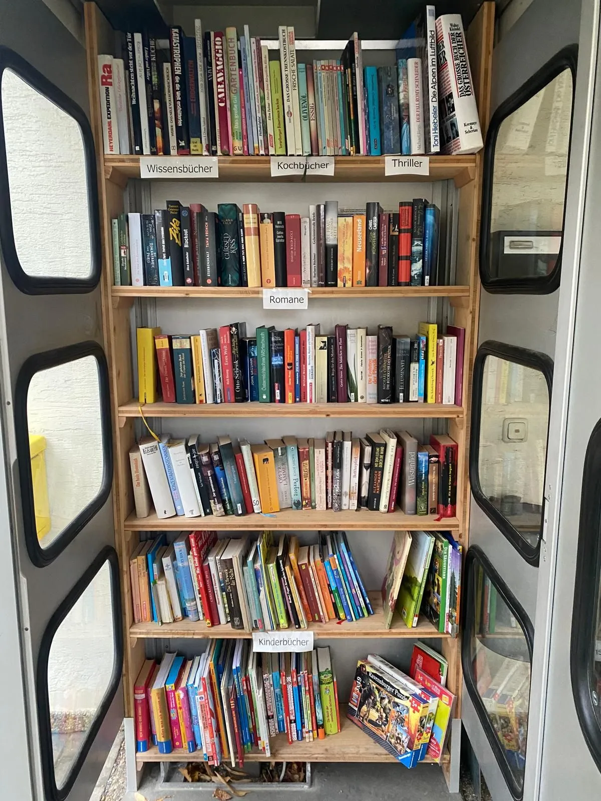 Ein hölzerne Bücherregal mit Büchern, nach Genre kategorisiert, in einem Fahrzeug.