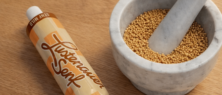 Eine 'Sennep'-Senftube neben einem Mörser und Stößel, gefüllt mit Senfkörnern.