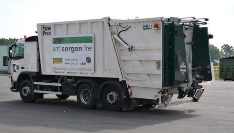 Ein weißer Müllwagen mit grünen und roten Akzenten, geparkt in einem Außenbereich. Der Lkw hat ein Motto 'ent sorgen frei' an seiner Seite.