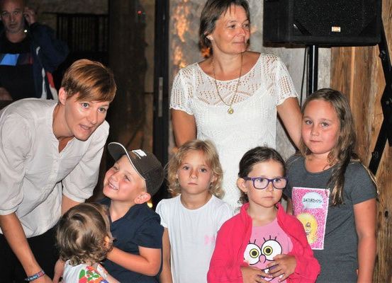 Eine Gruppe von Erwachsenen und Kindern lächelt für ein Foto. Die Frau in der Mitte trägt eine Halskette.