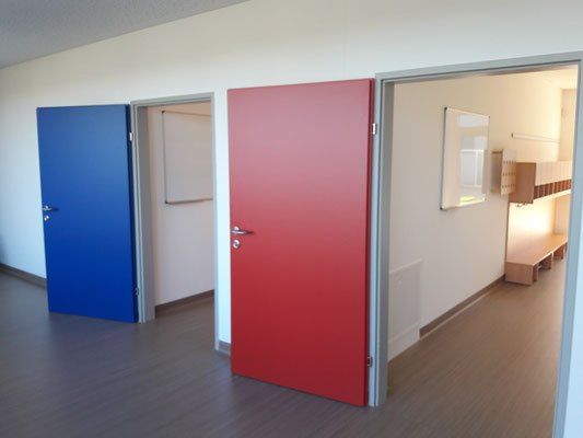 Ein leerer Raum mit drei Türen: eine blaue, eine rote und eine weiße. Die rote Tür ist offen und zeigt ein Fenster.